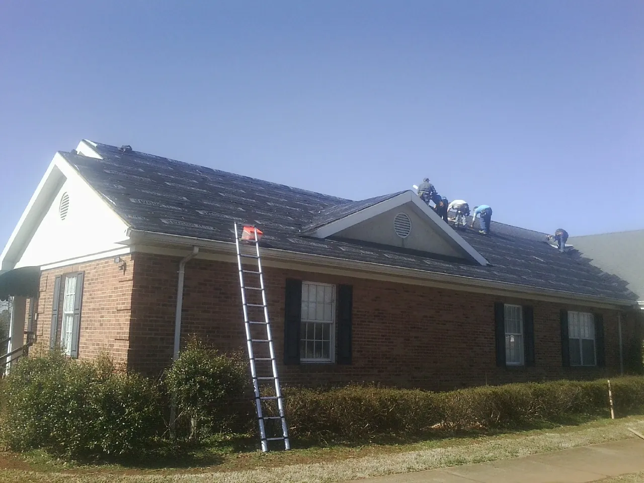 Crew tearing shingles off a brick ranch roof with a ladder set — Metal Roof Repair work by our crew in Warrenton