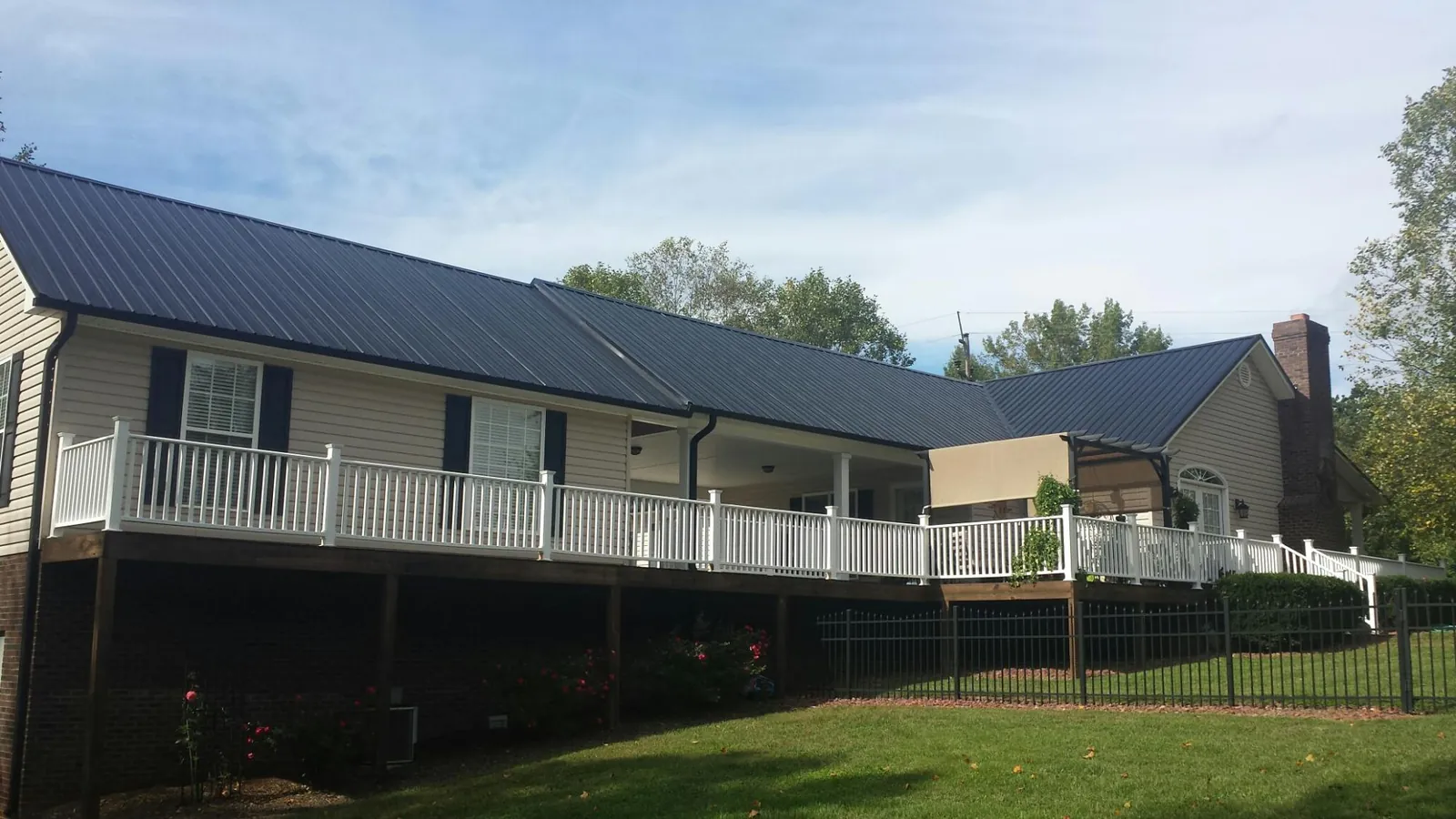 Black metal roof above a long white railed deck on a hillside home in Warrenton